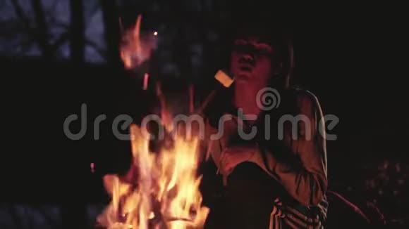 女孩晚上坐在炉火旁吹在棉花糖上视频的预览图