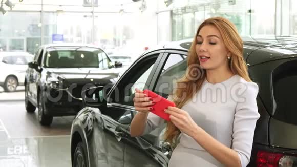 漂亮的幸福女人在经销商的新车附近自拍视频的预览图