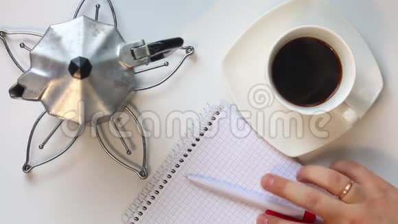 一个男人从桌子上的杯子里喝咖啡然后他拿起一支笔思考在笔记本上写什么在我的桌子旁边视频的预览图