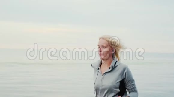 活跃的中年妇女女人在平静的大海或湖泊的背景下慢跑视频的预览图
