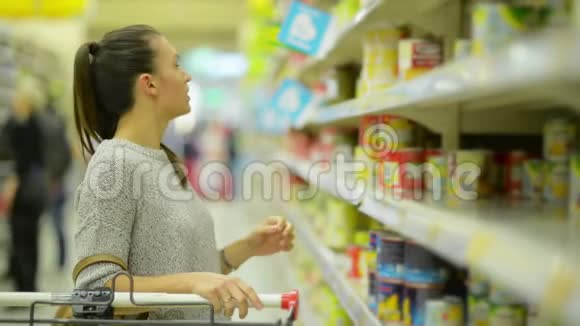 穿休闲服装的年轻妻子正在超市货架旁选择食品视频的预览图
