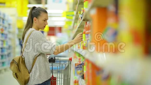 站在货架附近的超市里长着深色头发和购物车的女人买果汁视频的预览图