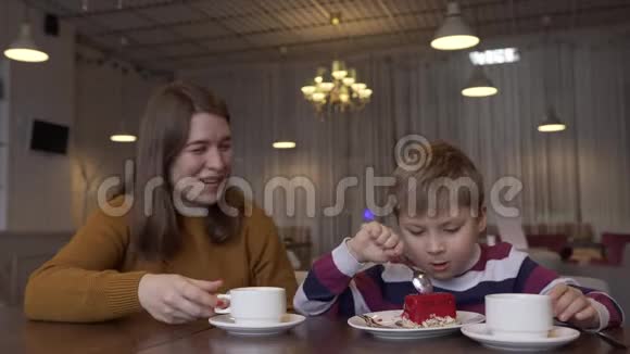 有趣的小男孩和漂亮的年轻妈妈喝茶吃蛋糕视频的预览图