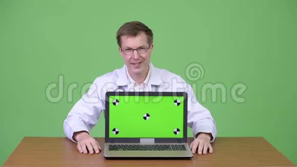医生边说话边坐着展示绿色屏幕笔记本电脑视频的预览图