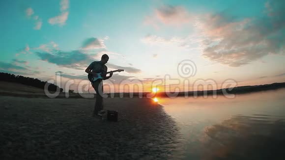 日落时分一位音乐家吉他手在水边弹奏电吉他男吉他手概念视频的预览图