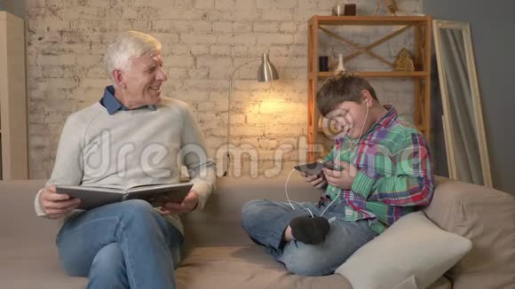 代的差异老人坐在沙发上看书一个年轻的胖子用平板电脑和视频的预览图