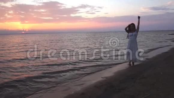 日落时分美丽的黑发少女在海滩上散步视频的预览图