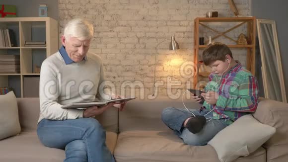 代的差异老人坐在沙发上看书一个年轻的胖子用平板电脑和视频的预览图