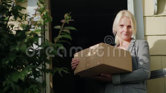 一个拿着包裹的女人站在她家的门槛上看着相机微笑着将包裹送达视频的预览图