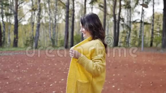 一个穿着黄色毛衣的年轻女子在秋天公园散步黑发女人在寒冷的森林里晒太阳恋爱中的女人视频的预览图