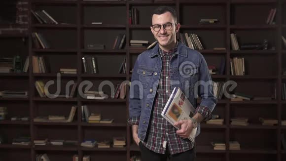 年轻的快乐男学生在图书馆的书架前拿书视频的预览图