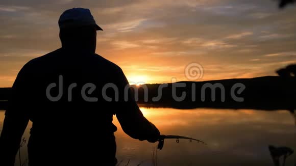 日落时湖岸上拿着钓竿的渔夫那个人在鱼饵上钓到了鱼视频的预览图