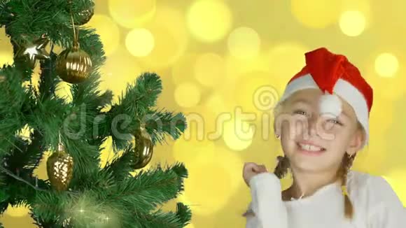 圣诞老人戴着红帽子在圣诞树旁跳舞的快乐少女快乐的年轻白种人女孩室内摄影棚特写镜头视频的预览图