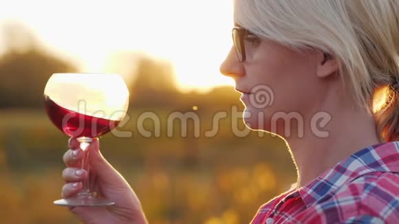一个女人正在品尝红酒日落时分站在葡萄园旁边的酒杯视频的预览图