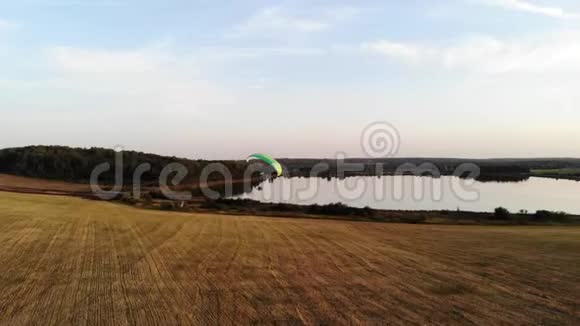 一架机动滑翔伞在田野上逆湖飞行视频的预览图