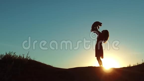 女孩举起一只小狗在日落剪影女人在大自然中和狗玩沉默的阳光友谊男人和视频的预览图