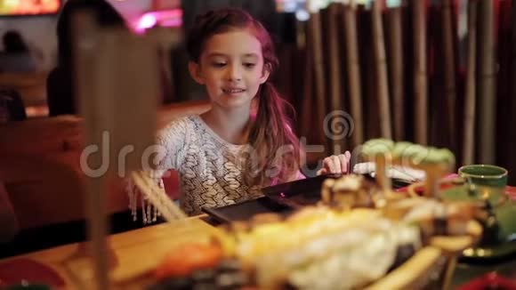 餐厅里可爱的小女孩搞笑地尝试用中国筷子吃寿司没有成功视频的预览图