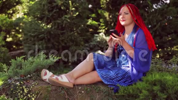 一个年轻的女人坐在公园的草地上用信使交流视频的预览图
