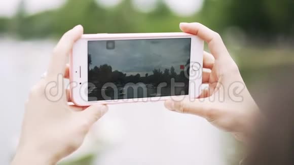年轻女子的手拿着智能手机在河边拍摄视频视频的预览图