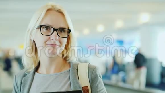 在机场大航站楼里穿西装戴眼镜的年轻女子在移动磁带上驾驶抵达新的地方视频的预览图
