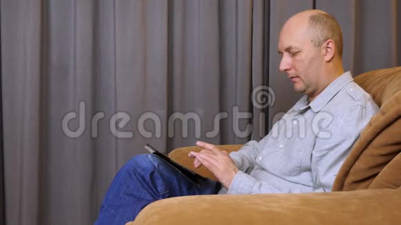 白人在平板电脑上打字成年男子坐在扶手椅上视频的预览图
