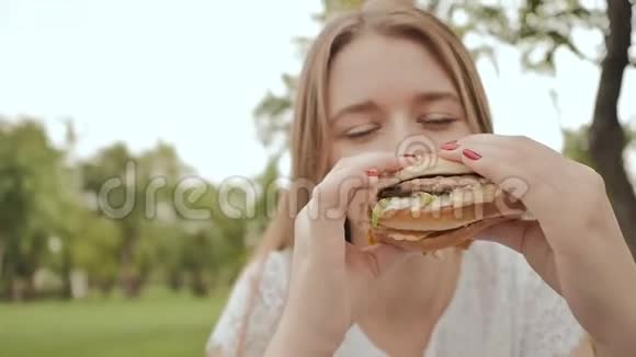 年轻的学生女孩在公园里户外吃汉堡包学习期间休息视频的预览图