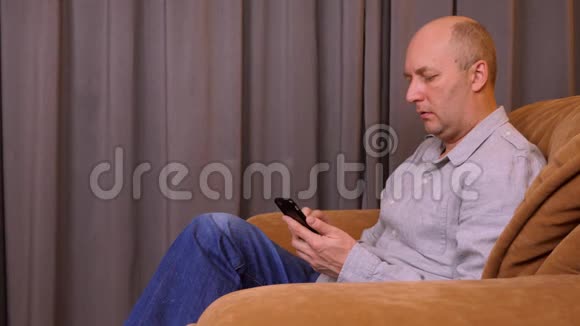 成年白种人坐在扶手椅上用手机读留言在家里视频的预览图