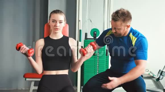 美女在健身房的私人教练的帮助下做举重运动视频的预览图