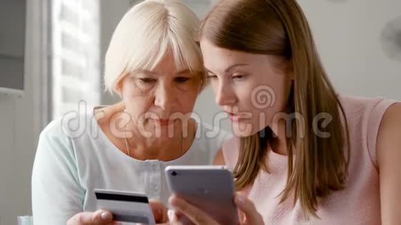 年长的母亲和她的小女儿在家里使用智能手机用信用卡买手机视频的预览图