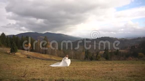 年轻迷人的新娘穿着时尚的婚纱正沿着山间金色的草地奔跑视频的预览图