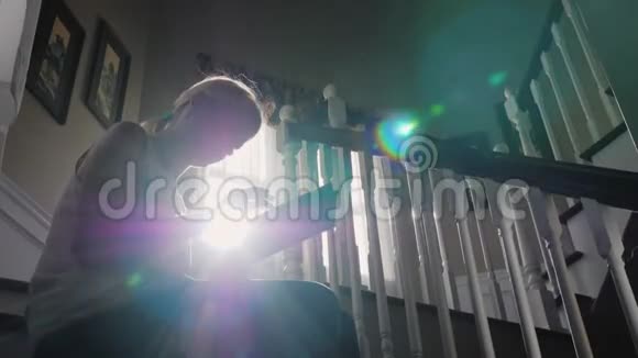 一个年轻的女人正在用平板电脑工作坐在家里的楼梯上剪影阳光照在身后视频的预览图