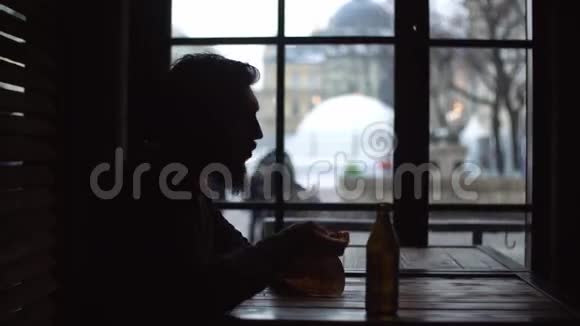 一个年轻人在窗边的酒吧喝啤酒吃零食的剪影视频的预览图