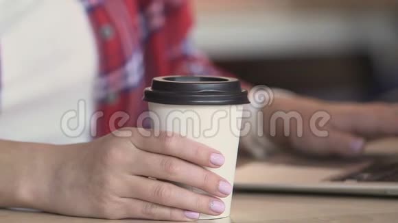 年轻女士喝着纸杯里的咖啡看着笔记本电脑上的新闻提要视频的预览图