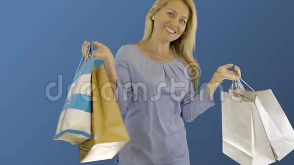 年轻的白种人女人带着购物袋在蓝色的后院旋转购物后快乐的金发女孩视频的预览图