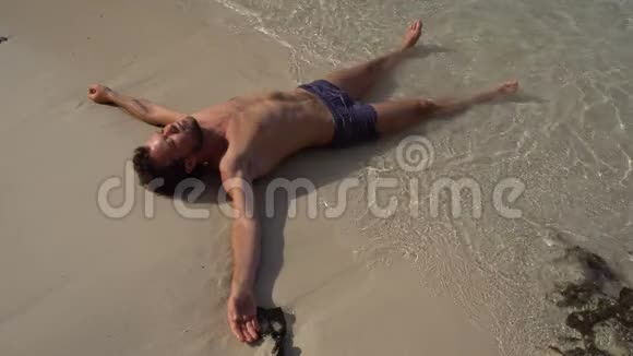 放松的人躺在白色的沙滩上用温暖的蔚蓝的海水冲洗视频的预览图