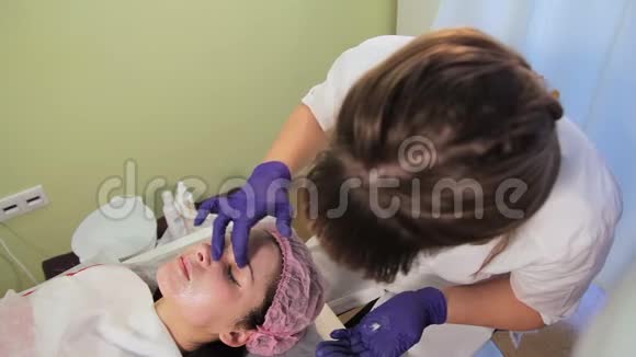 美容师在女人的脸上涂了一层舒缓霜中胚层治疗后皮肤发红发炎辉光视频的预览图