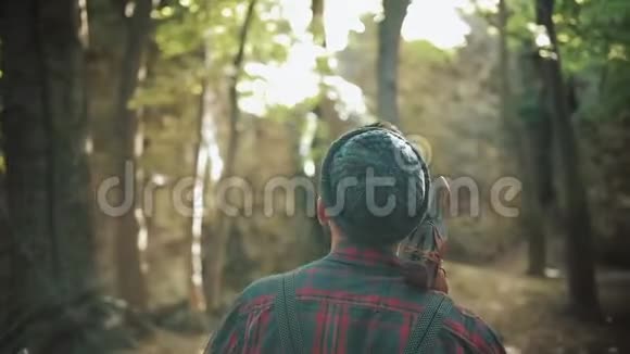带着斧头走着长胡子的伐木工人戴帽子的人穿过树林寻找那棵树后面的景色视频的预览图