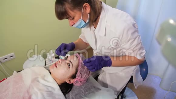 美容师从女人的脸上摘下面具治疗后皮肤发红刺激Bb发光视频的预览图