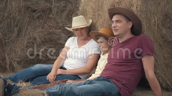 幸福的家庭母亲父亲和儿子拿着一块石板坐在地里靠在干草卷上快乐的概念视频的预览图