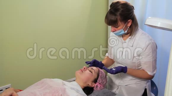 美容师在女人的脸上涂了一层舒缓霜中胚层治疗后皮肤发红发炎辉光视频的预览图