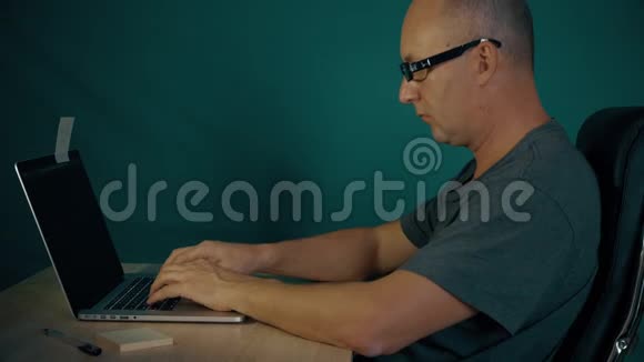 程序员坐在桌子旁在笔记本电脑上编码人指手在键盘上快速打字侧视坐着视频的预览图
