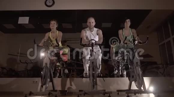 三名健身者在夜间一起骑固定自行车训练的肖像视频的预览图