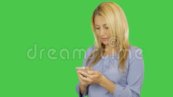 年轻女子在绿色屏幕的智能手机上键入短信年轻女子站着用手机阿尔法通道视频的预览图