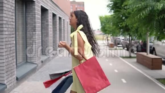 一个穿着黄色连衣裙的黑发迷人的年轻女孩购物后心情愉快慢动作视频的预览图
