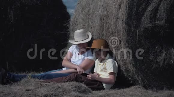 幸福的家庭母子带着平板电脑坐在田里靠在干草卷上幸福家庭的概念视频的预览图