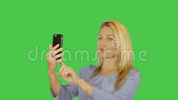 金发年轻女子正在智能手机透明绿色屏幕背景上拍照自我肖像阿尔法频道视频的预览图