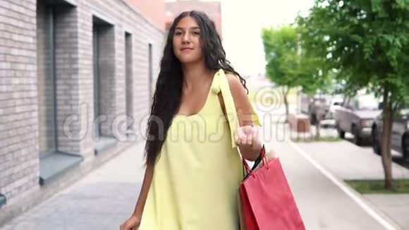 一个穿着黄色衣服的漂亮女孩在购物后走在街上慢动作视频的预览图