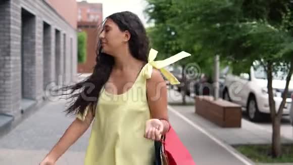 快乐的年轻女孩黑发穿着黄色长裙购物后心情愉快慢动作视频的预览图