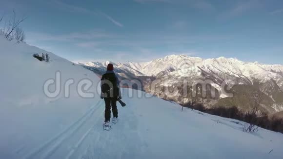 跟随女摄影师徒步旅行和步行雪鞋在雪地小径在冬天高山雪山视频的预览图