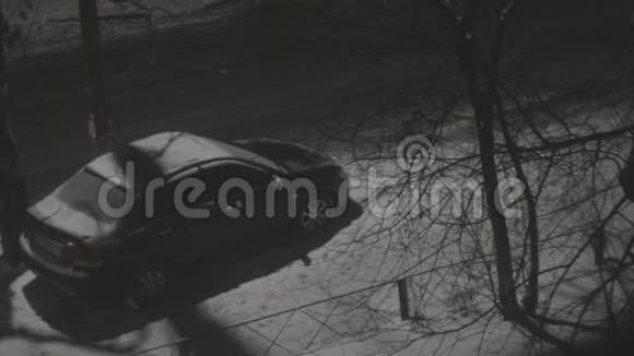 在冬天的雪夜路灯柱下人们在停放的汽车旁行走视频的预览图